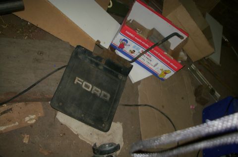 1981 Ford Bronco - A black Ford mud flap lies on the floor amidst clutter and cardboard boxes.