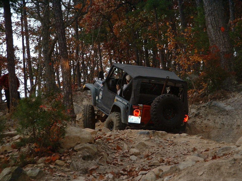 Gray Jeep Wrangler flexing over rock ledge at dusk, three-quarter rear view