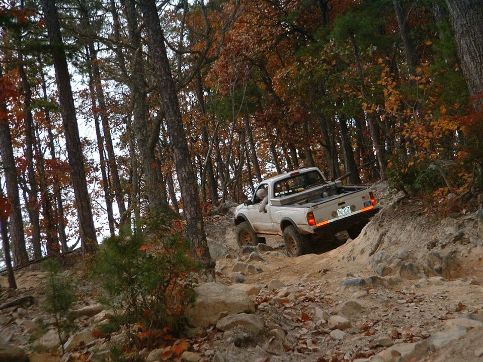 White pickup truck driving on a rocky, wooded trail