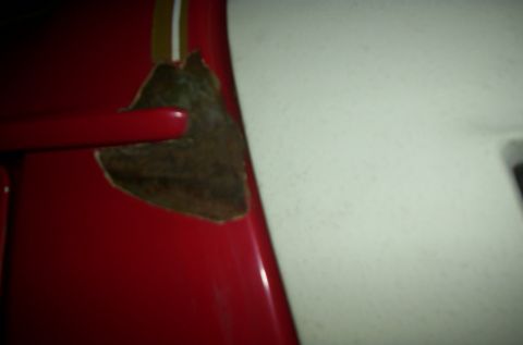 1981 Ford Bronco - Close-up of a red vehicle panel showing rust damage and a partial yellow stripe.