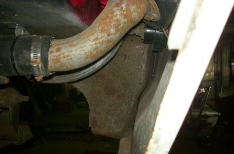 1981 Ford Bronco - Close-up view of a corroded metal pipe and bracket on a vehicle's undercarriage.