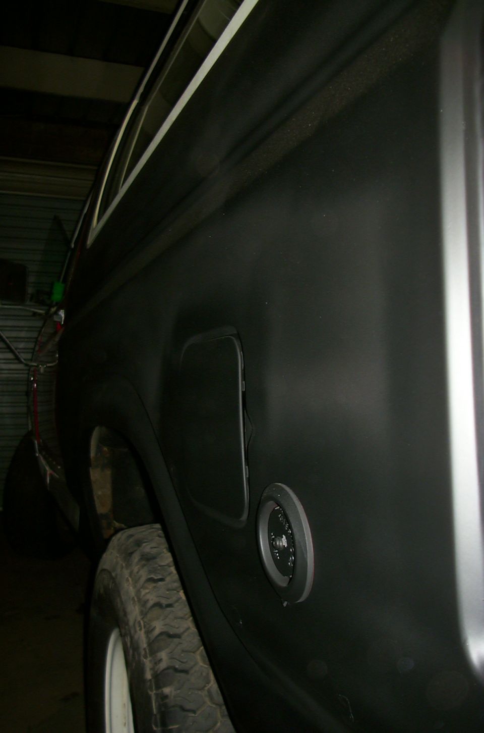 Vehicle rear quarter panel showing fuel door and gas cap. Tire visible