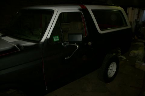 1981 Ford Bronco - A black Ford Bronco with a white roof and a red stripe is parked indoors.
