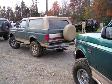 1996 Ford Bronco - A green and tan 1996 Ford Bronco is parked next to another vehicle, with a spare tire mounted on the rear.