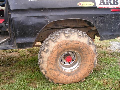 1996 Ford Bronco - Close-up of a large, mud-caked tire on a vehicle, parked on a grassy area.