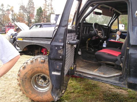 1996 Ford Bronco - The interior of a modified off-road Bronco, likely from the late 1970s, is shown with its door open.
