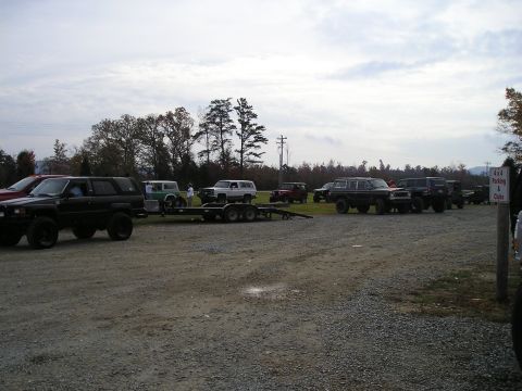 1996 Ford Bronco - A collection of off-road vehicles are gathered in an outdoor lot under a cloudy sky.