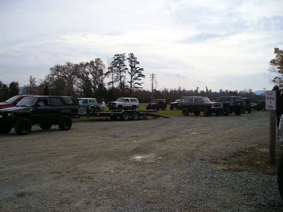 Several SUVs and trucks parked in a gravel lot with trees in the background