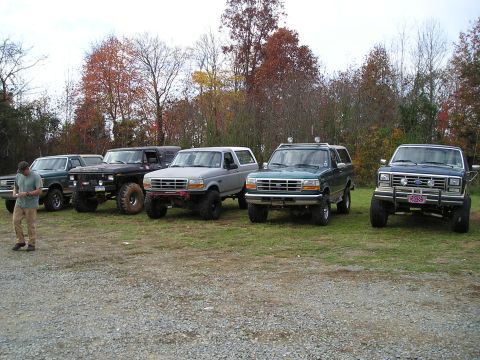 1996 Ford Bronco - A group of Ford Bronco SUVs are lined up in a gravel lot, with a man standing near the leftmost vehicle.