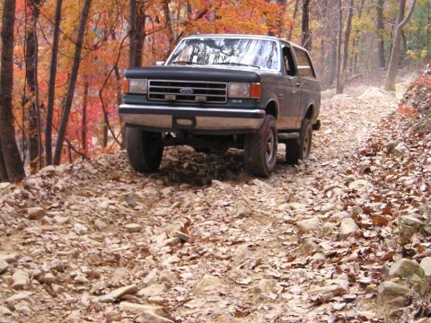 1996 Ford Bronco - A Ford Bronco navigates a challenging off-road path surrounded by colorful fall foliage.