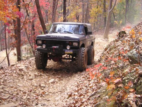 1996 Ford Bronco - Off-road SUV navigating a wooded trail during autumn.