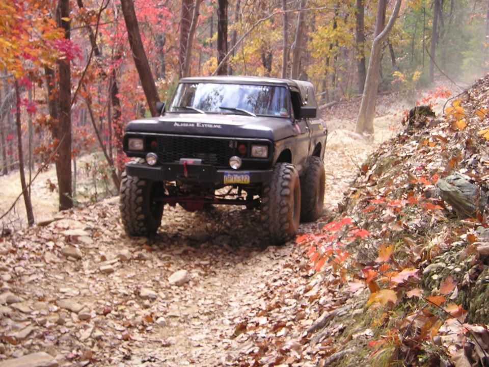 Black off-road SUV with large tires on a rocky, leaf-covered trail in the woods