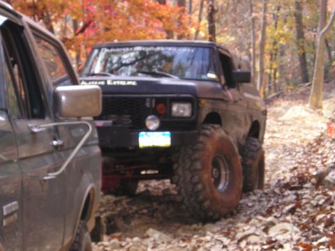 1996 Ford Bronco - Two modified SUVs navigate a wooded trail during autumn, with one vehicle in the foreground and another in the background.