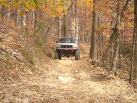 1996 Ford Bronco - A silver Ford Bronco navigates a rocky, leaf-strewn path through an autumn forest.