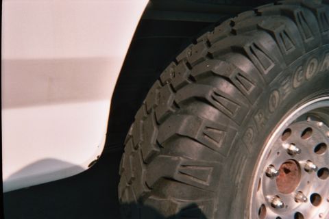1990 Ford Bronco - Close-up of a Pro Comp mud-terrain tire and polished wheel against a white vehicle body.