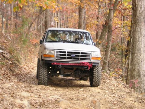 1996 Ford Bronco - 1996 Ford Bronco navigates a rough, leaf-covered path through an autumn forest.