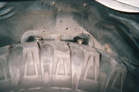 1990 Ford Bronco - mud-terrain tire tucked up into a fender well, viewed from below showing inner fender and hardware.