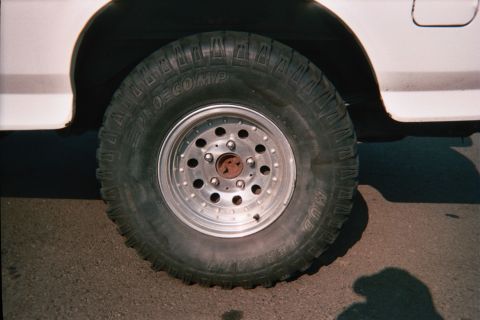 1990 Ford Bronco - Pro Comp mud-terrain tire on a polished aluminum wheel mounted under a white vehicle's fender.