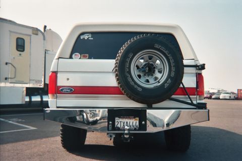 1990 Ford Bronco - Rear view of a white and red Ford Bronco with a rear-mounted spare tire and California plate, in a lot.