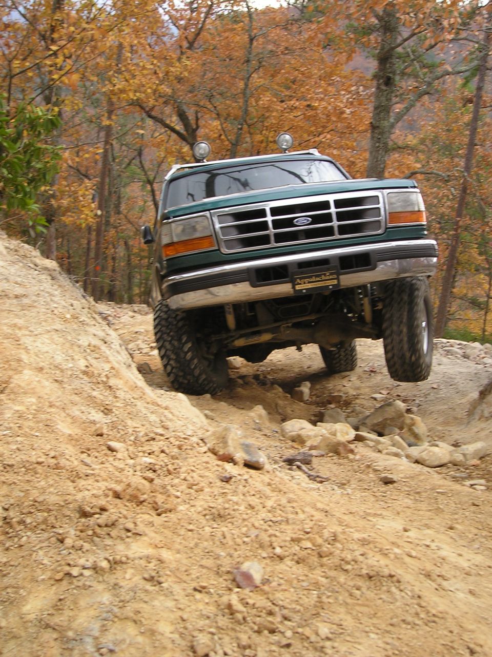 Green Ford Bronco climbing rocky trail with fall foliage in background