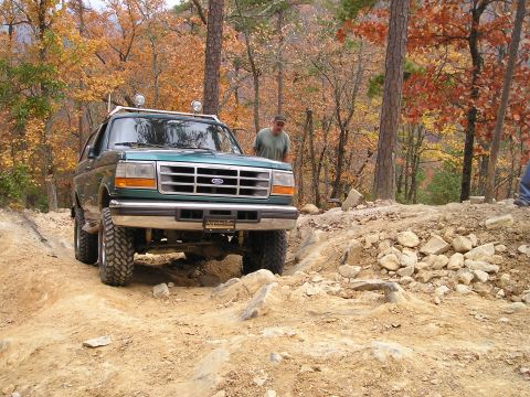 1996 Ford Bronco - A green Ford Bronco navigates a rocky, off-road trail during autumn.