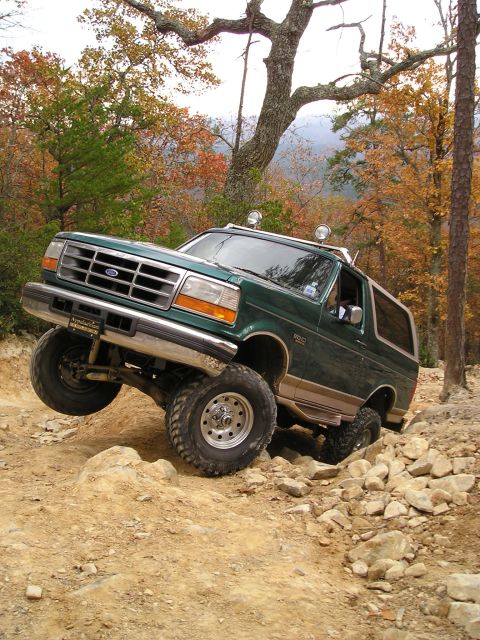 1996 Ford Bronco - A green 1996 Ford Bronco tackles a challenging rocky trail, its off-road capabilities amidst a backdrop of fall colors.