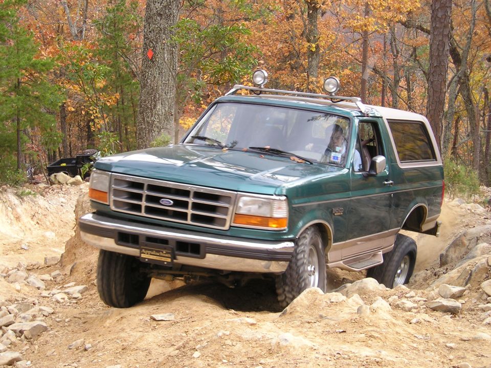 Green 1996 Ford Bronco driving on a dirt trail with trees and fall foliage