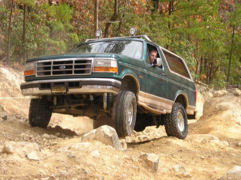 1996 Ford Bronco - 1996 Ford Bronco navigating a rocky off-road trail with trees in the background.