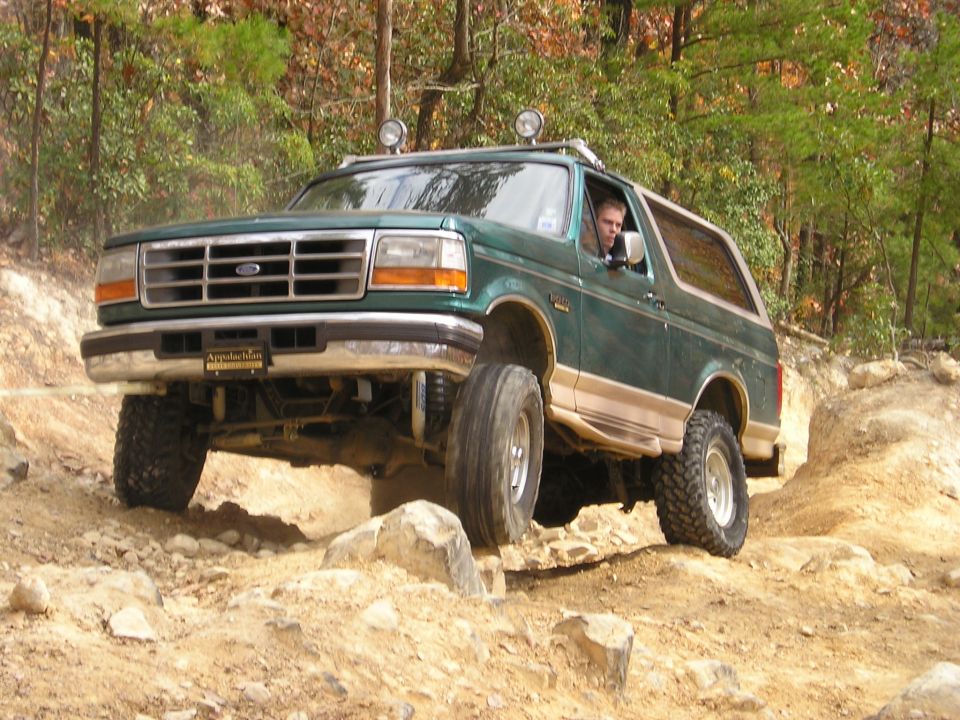 Green 1996 Ford Bronco with tan trim driving over rocks on a dirt trail