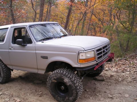1996 Ford Bronco - A silver Ford Bronco with off-road modifications is seen on a wooded trail during autumn.