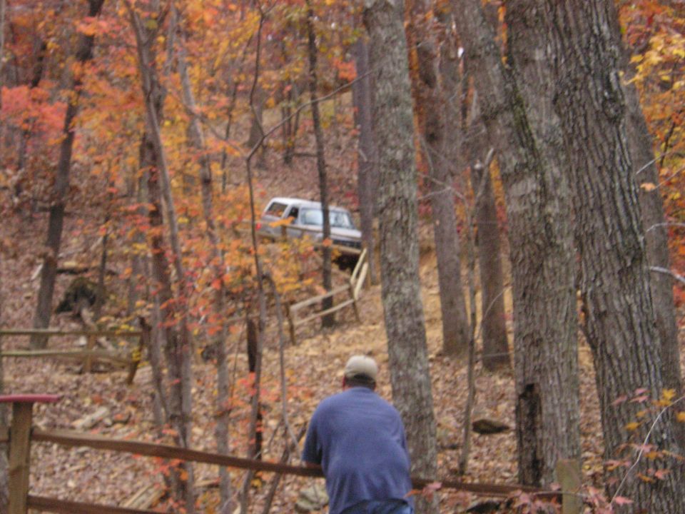1996 Ford Bronco driving up a wooded hill with fall foliage