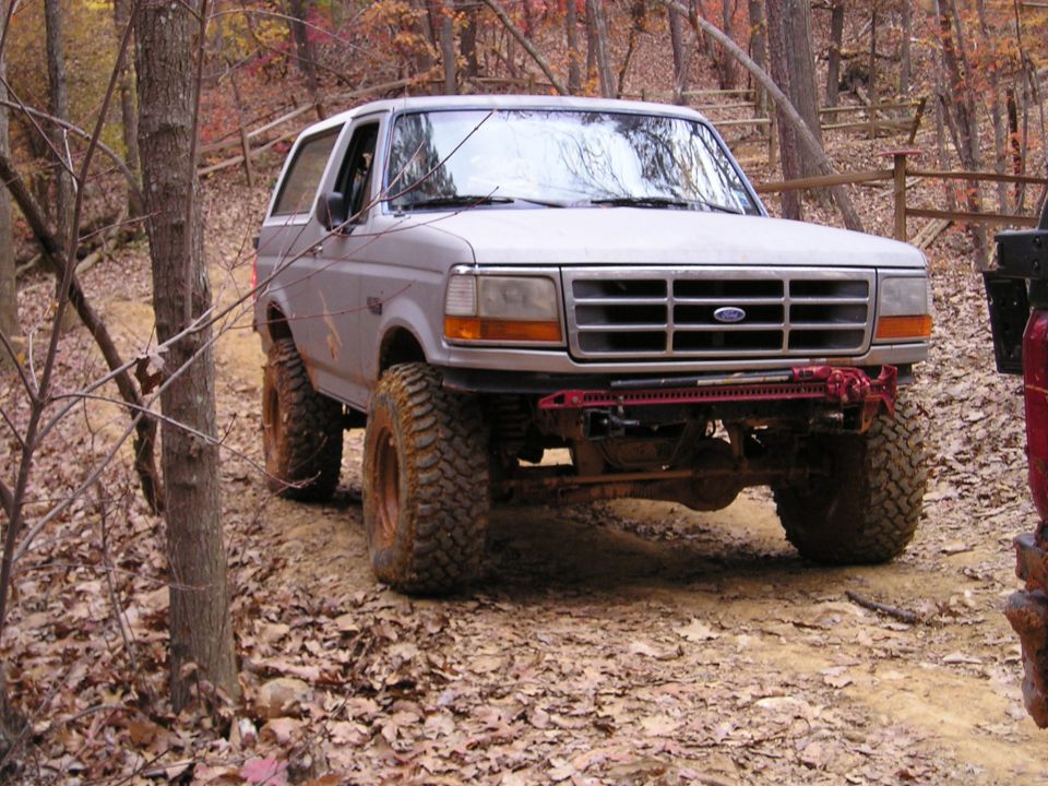 Gray 1996 Ford Bronco with large tires on a wooded trail
