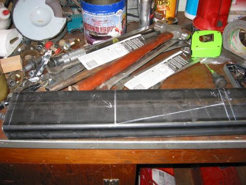 1985 Ford Bronco - A metal part is marked with lines and measurements on a cluttered workbench with various tools.