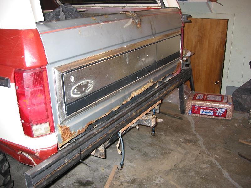 Rusted-out tailgate removed from red and white SUV propped in garage during bodywork
