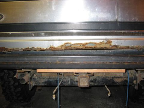 1985 Ford Bronco - The rear bumper of a silver SUV shows extensive rust, with a trailer hitch receiver visible below.