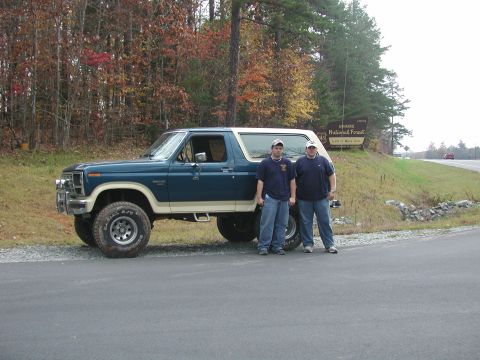 1985 Ford Bronco - A Ford Bronco is parked on the side of the road with two people standing next to it, in front of a national forest sign.