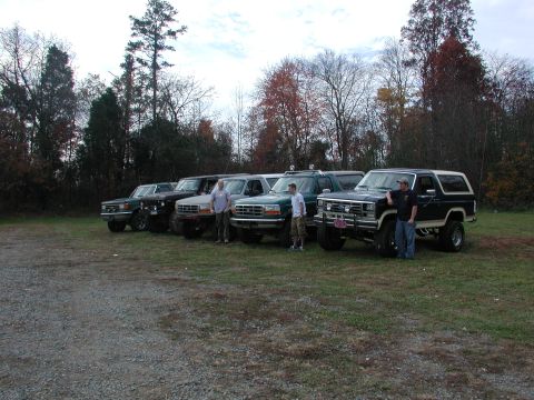 1985 Ford Bronco - Several Ford Broncos are lined up on a gravel lot with trees in the background.