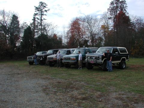 1985 Ford Bronco - A group of Ford Broncos and trucks are parked together on a gravel lot.