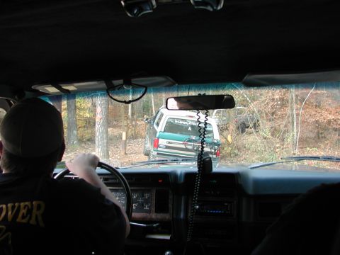 1985 Ford Bronco - Two SUVs navigate a wooded trail, with one vehicle visible ahead and another in the background.