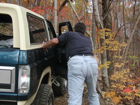 1985 Ford Bronco - A man approaches a dark teal and cream Ford Bronco in a forest during autumn.