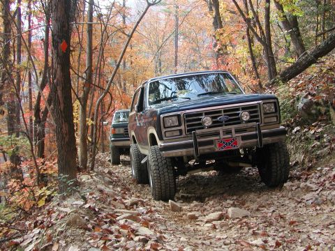 1985 Ford Bronco - A dark blue 1985 Ford Bronco navigates a rocky, wooded trail during autumn.