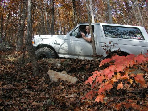1985 Ford Bronco - A man drives a white Ford Bronco through a wooded area during autumn, navigating fallen leaves and rocks.