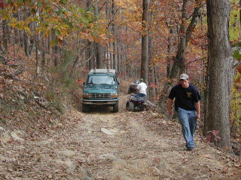 1985 Ford Bronco - A group of vehicles navigates a rough, off-road path through a forest during autumn.