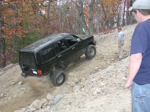 1985 Ford Bronco - A black SUV navigates a challenging off-road trail with onlookers present.