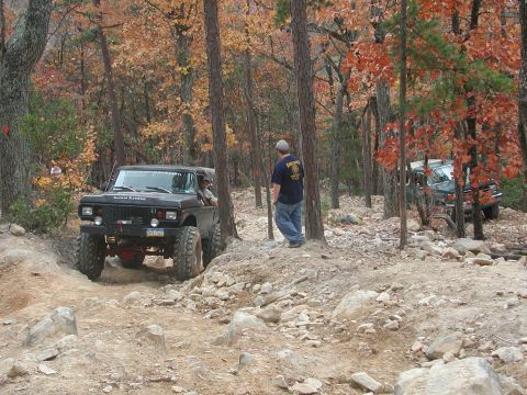 1985 Ford Bronco - A black Ford Bronco navigates a challenging off-road course with another vehicle visible in the background.