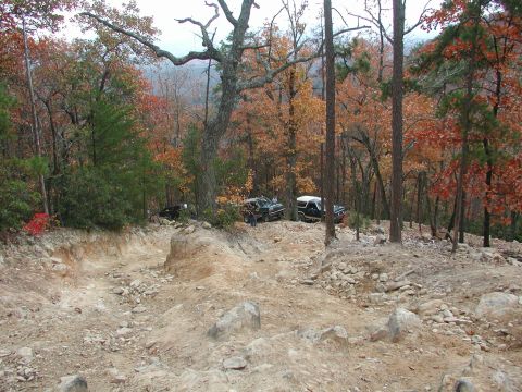 1985 Ford Bronco - Multiple off-road vehicles navigate a challenging dirt trail through a forest during autumn.