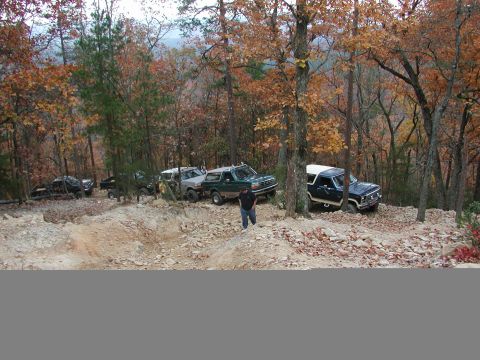 1985 Ford Bronco - A group of off-road vehicles, including a 1985 Ford Bronco, navigate a wooded trail during autumn.