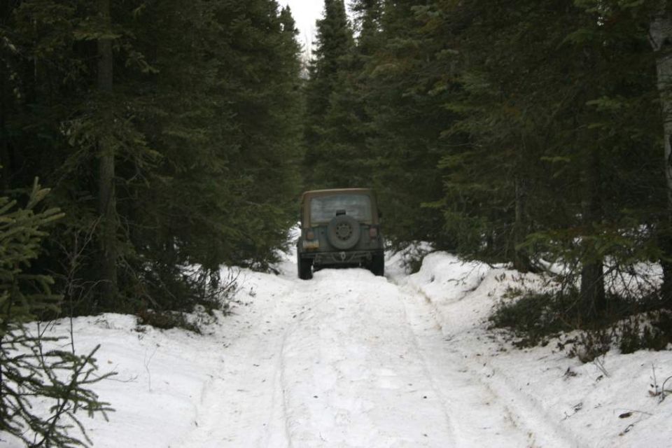 Brown Jeep TJ on snowy forest road, rear view