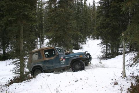 2003 Jeep TJ - A 2003 Jeep TJ navigates a snowy trail through a dense forest, with a tow rope attached.