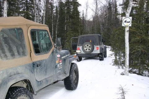 2003 Jeep TJ - Two Jeep Wranglers on a snowy forest trail, one parked in front of the other with its door ajar.